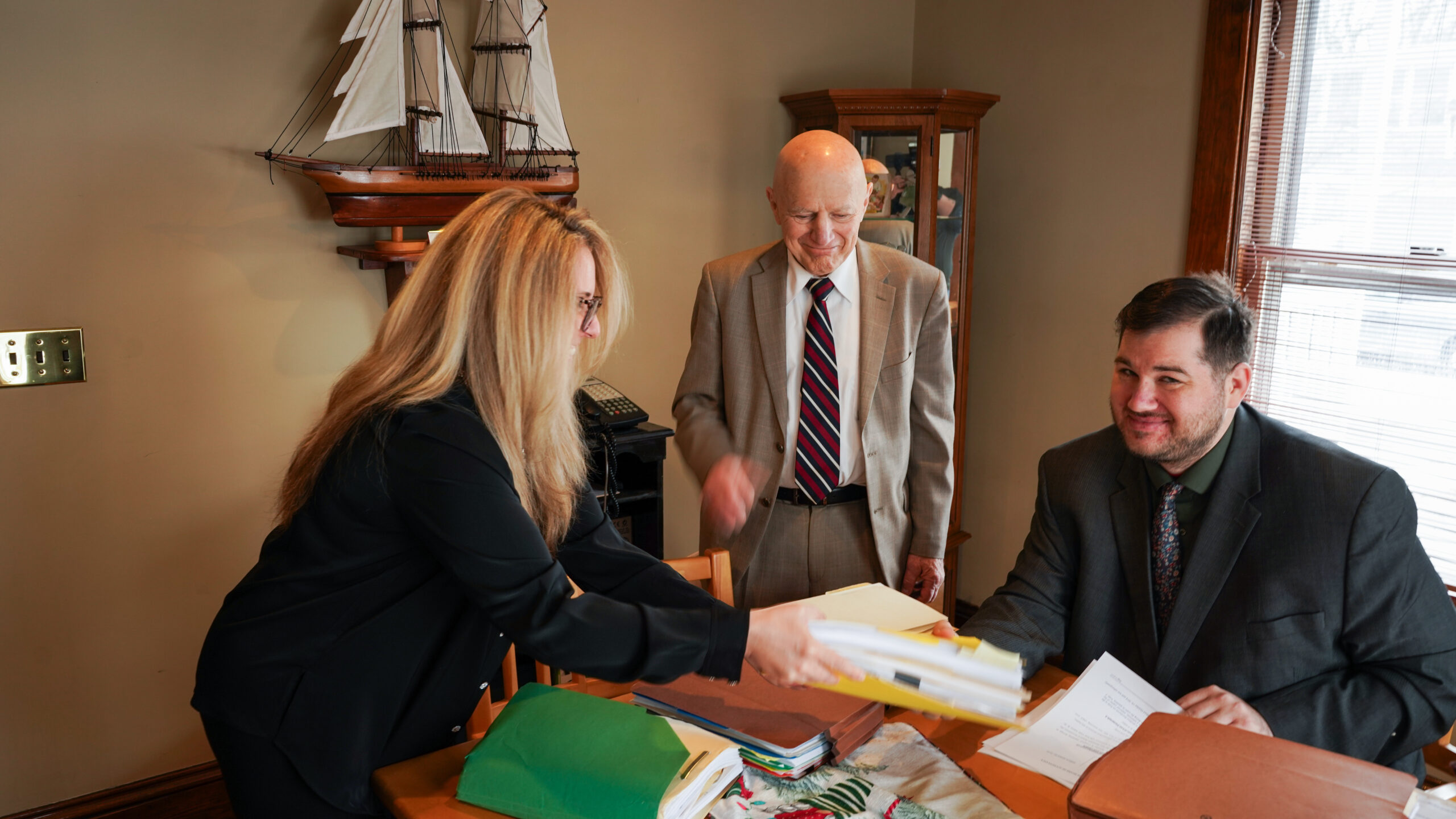 A group of four professionals, two men and two women, are gathered around a conference table reviewing printed charts and documents.