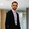 Business professional in a black jacket and glasses standing in a bright modern office hallway