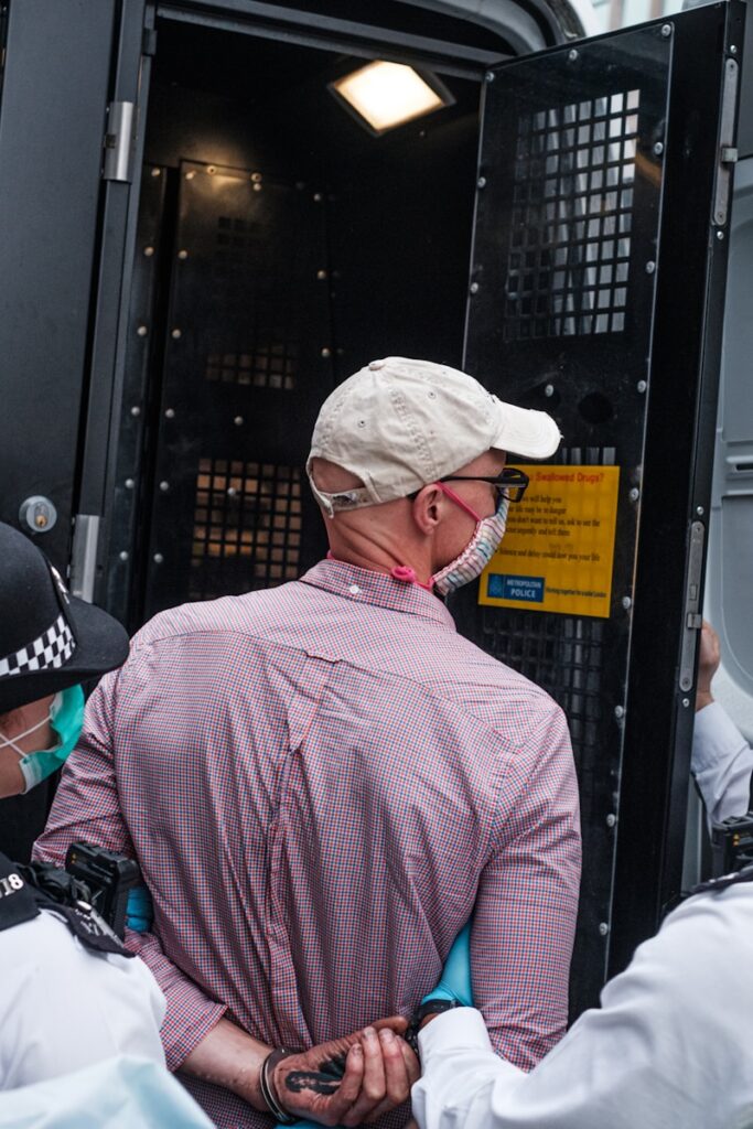 man in red and white plaid dress shirt wearing white knit cap representative of an immigrant being brought into custody by Immigration and Customs Enforcement (ICE)